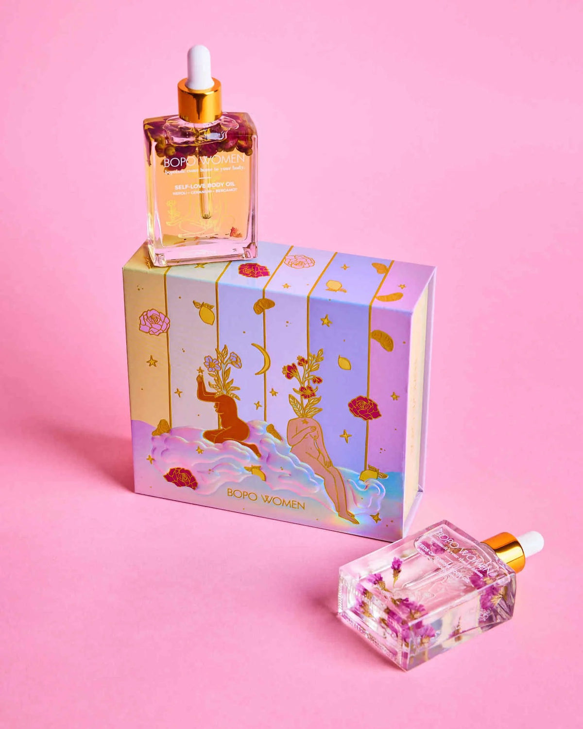 Two decorative bottles with droppers and a colorful box on a pink background