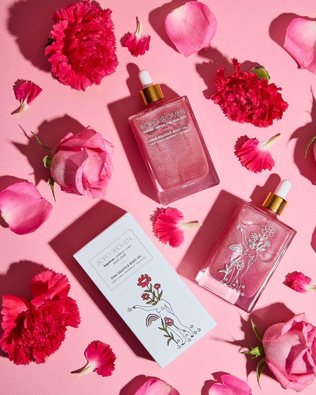 Two skincare bottles with droppers and a box on a pink background with flowers.