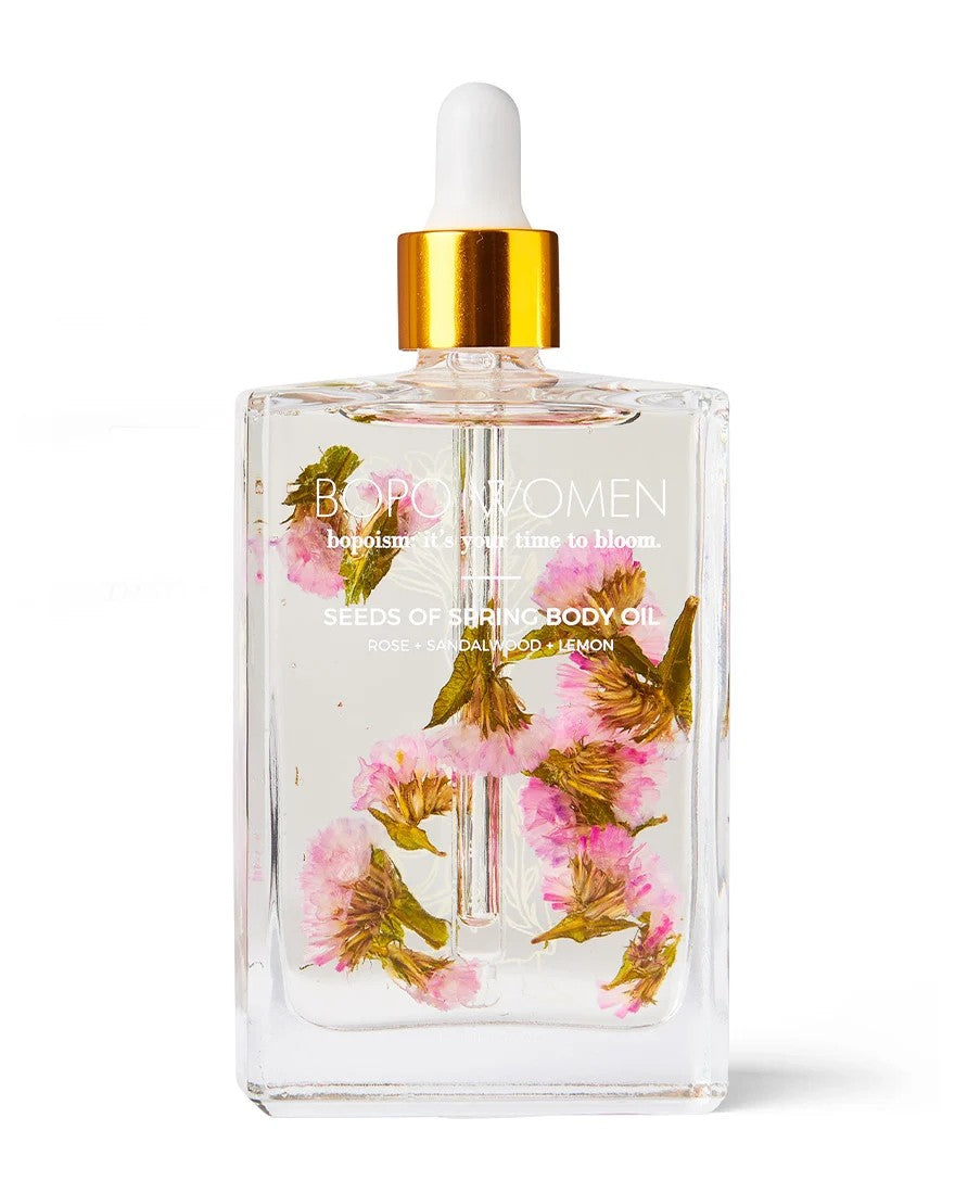 BOPO Women's body oil bottle with packaging and pink flowers on a white background