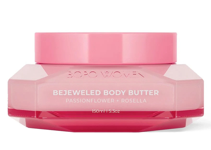 A jar of BOPO WOMEN Bejeweled Body Butter in a translucent pink glass container, displayed in front of its matching pink packaging box on a solid pink background.