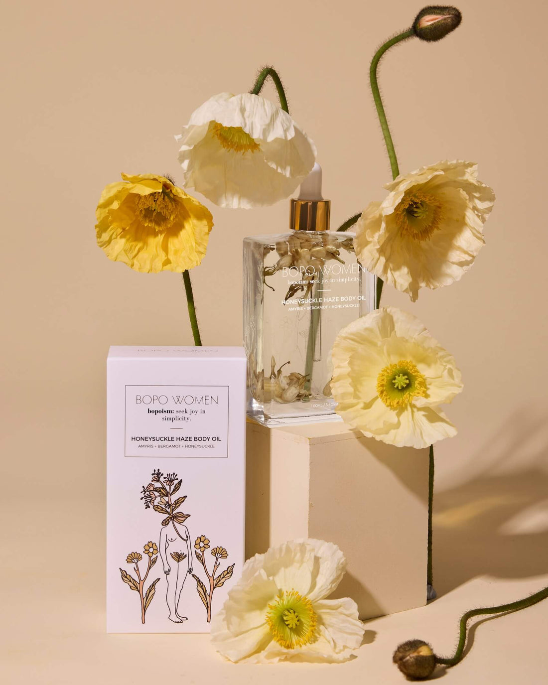 Clear glass bottle with gold cap, white box labeled 'Boro Women', and yellow flowers on a beige background