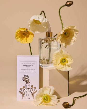 Clear glass bottle with gold cap, white box labeled 'Boro Women', and yellow flowers on a beige background