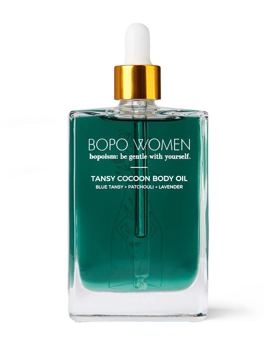 Bottle of BORO Women's body oil with flowers on a blue background