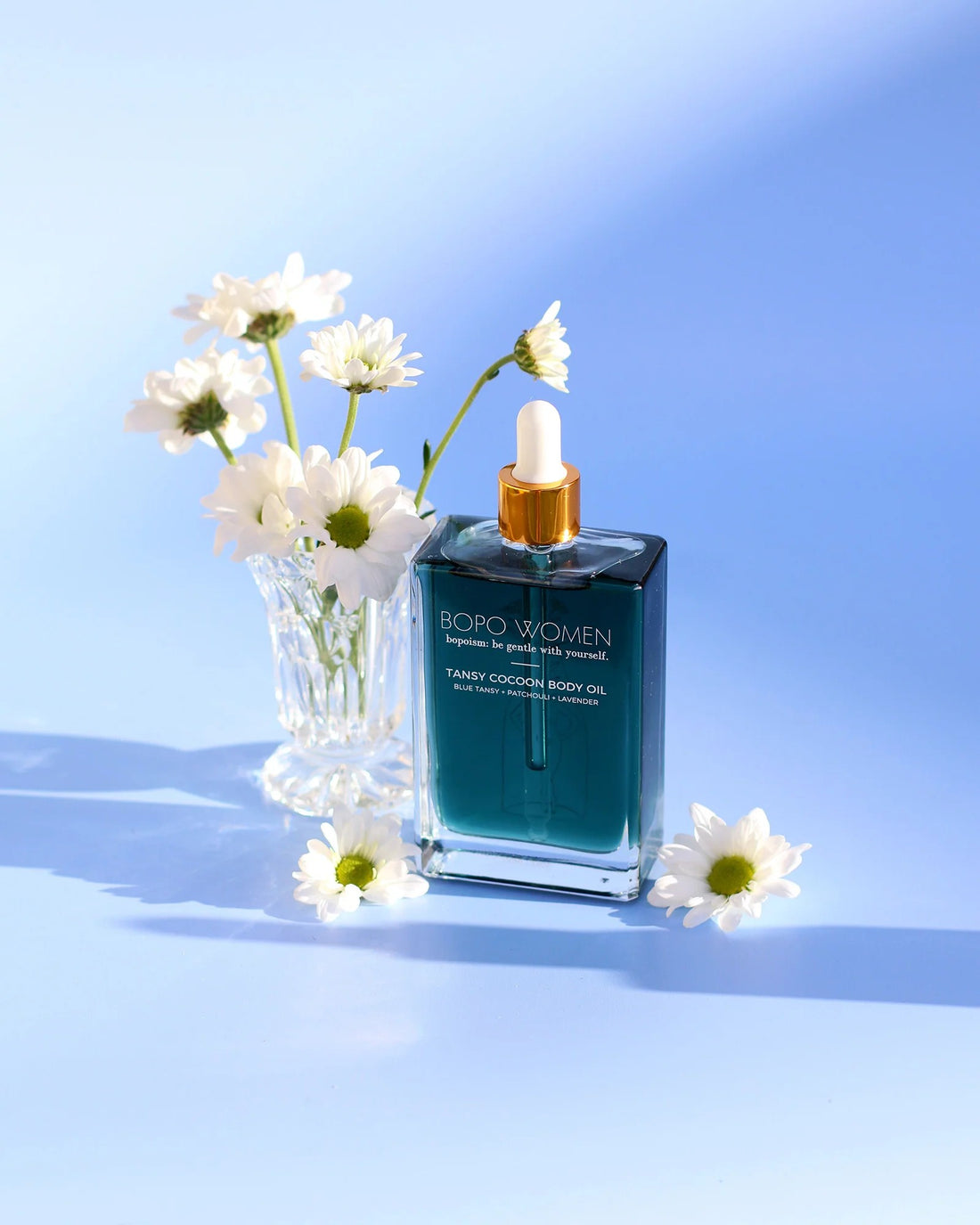 Bottle of BORO Women's body oil with flowers on a blue background
