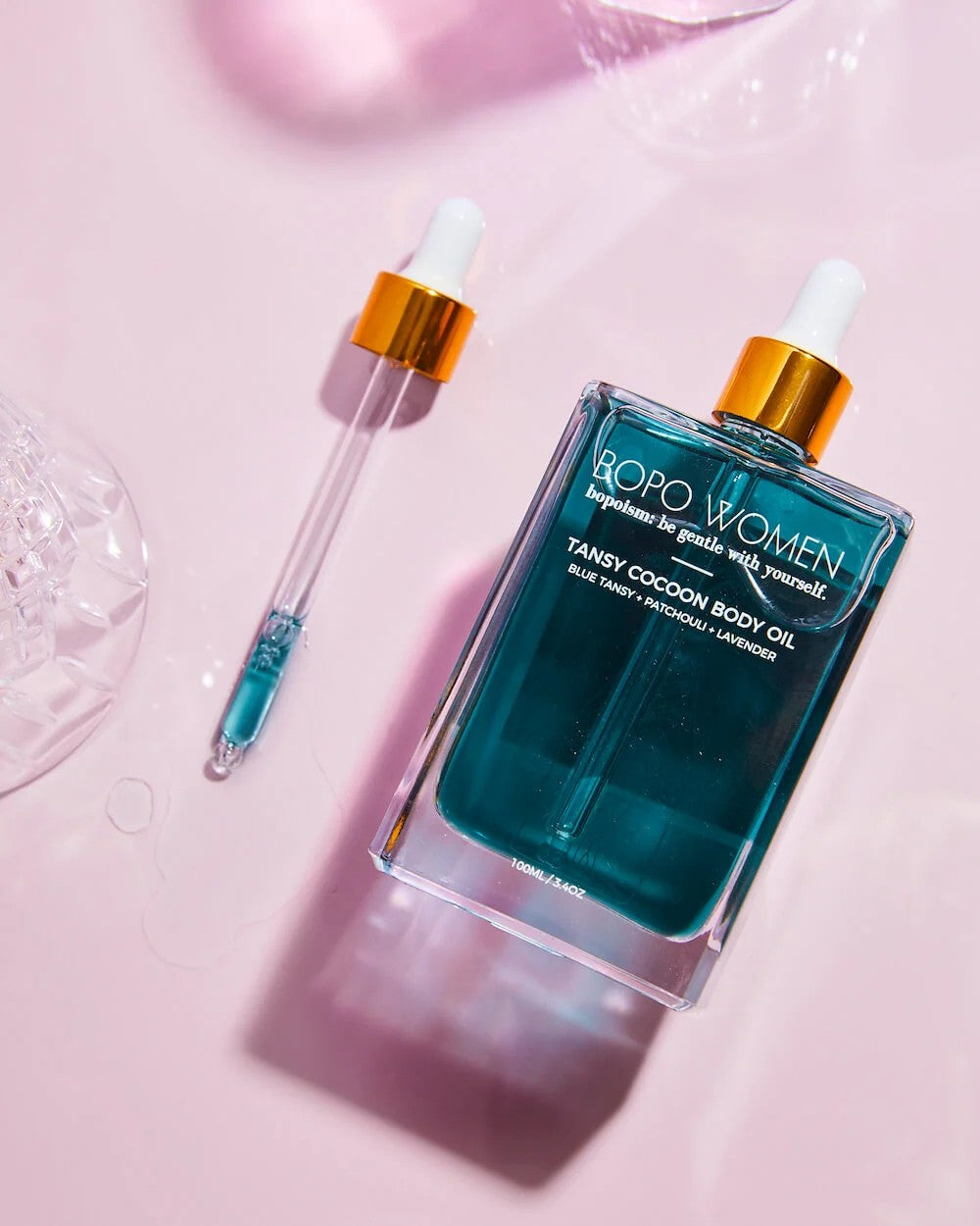 Blue bottle of body oil with dropper on a pink background