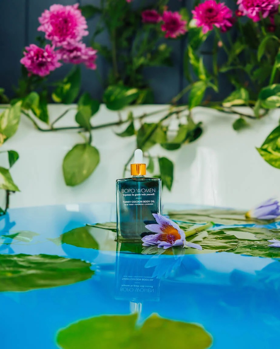 Cosmetic bottle with dropper on a reflective water surface with flowers in the background