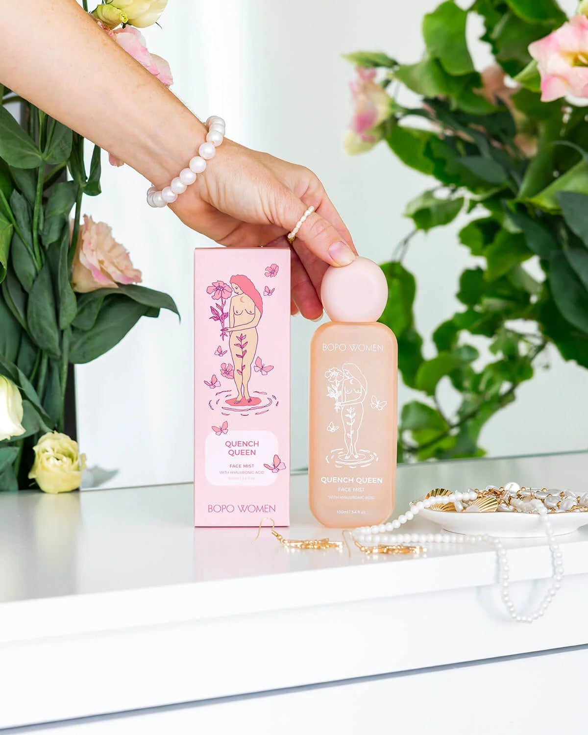 Hand holding a pink bottle with packaging labeled 'Quench Queen' against a floral background