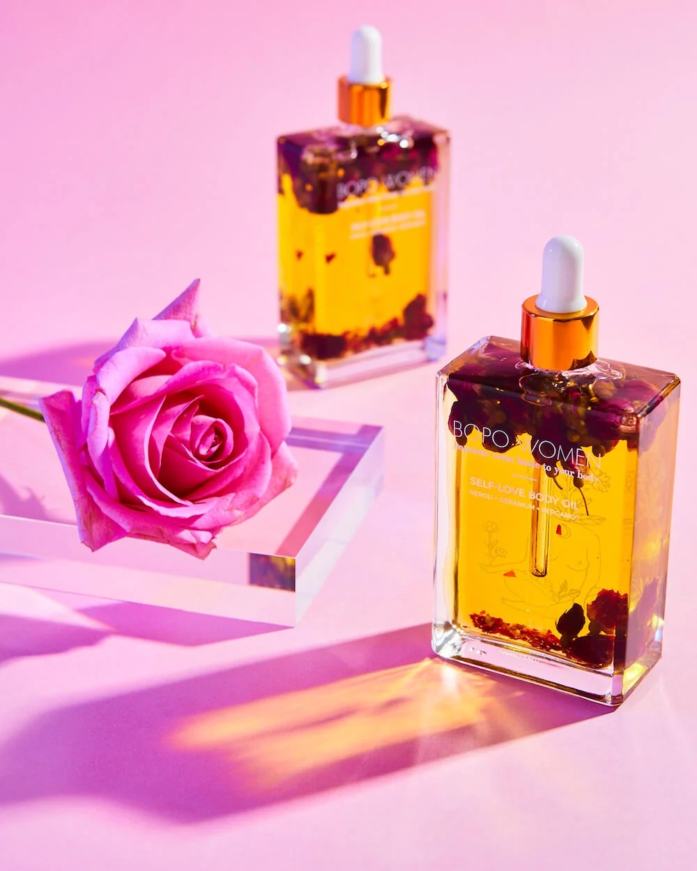 Two bottles of BORO & ROME essential oils with a pink rose on a pink background