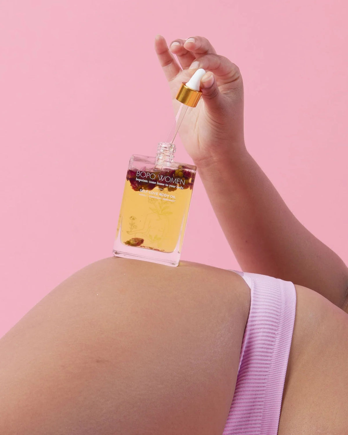 Hand applying perfume to a person's back against a pink background