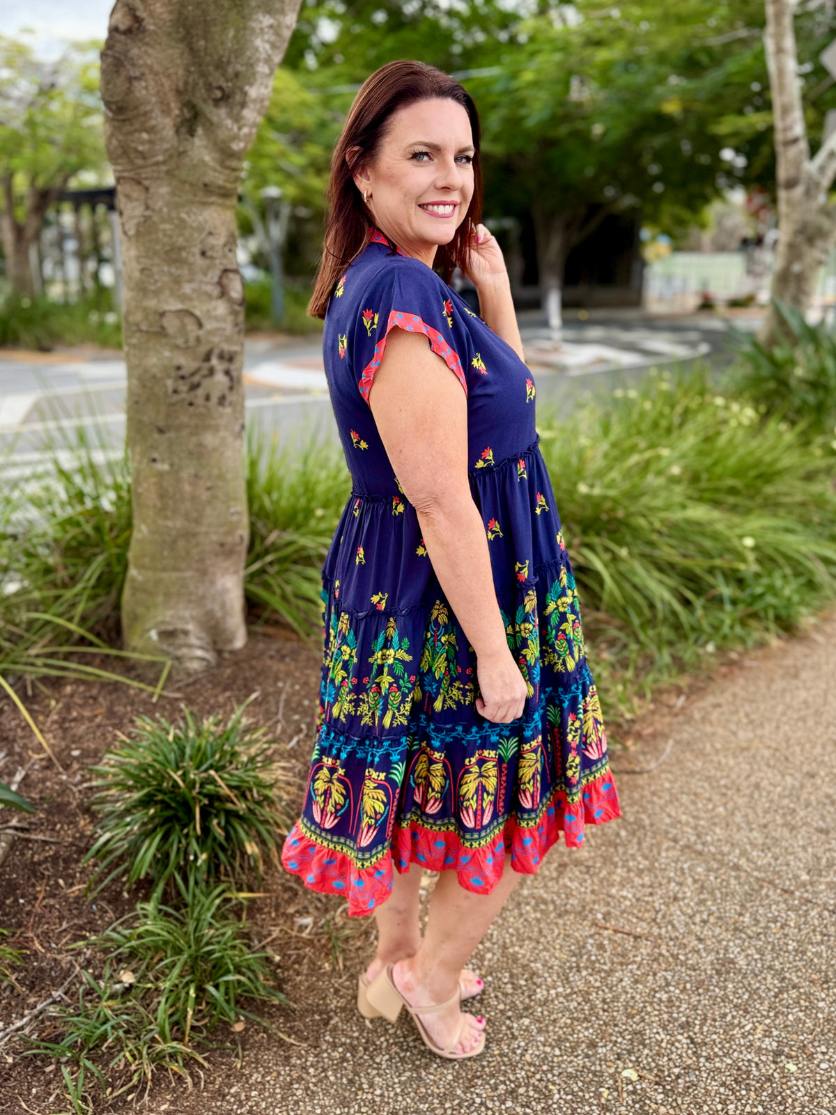  short-sleeve tiered dress with a navy blue base and coluorful bohemian-style floral and geometric patterns in red, green, yellow, and orange. The dress features a red and yellow patterned V-neckline and hem.