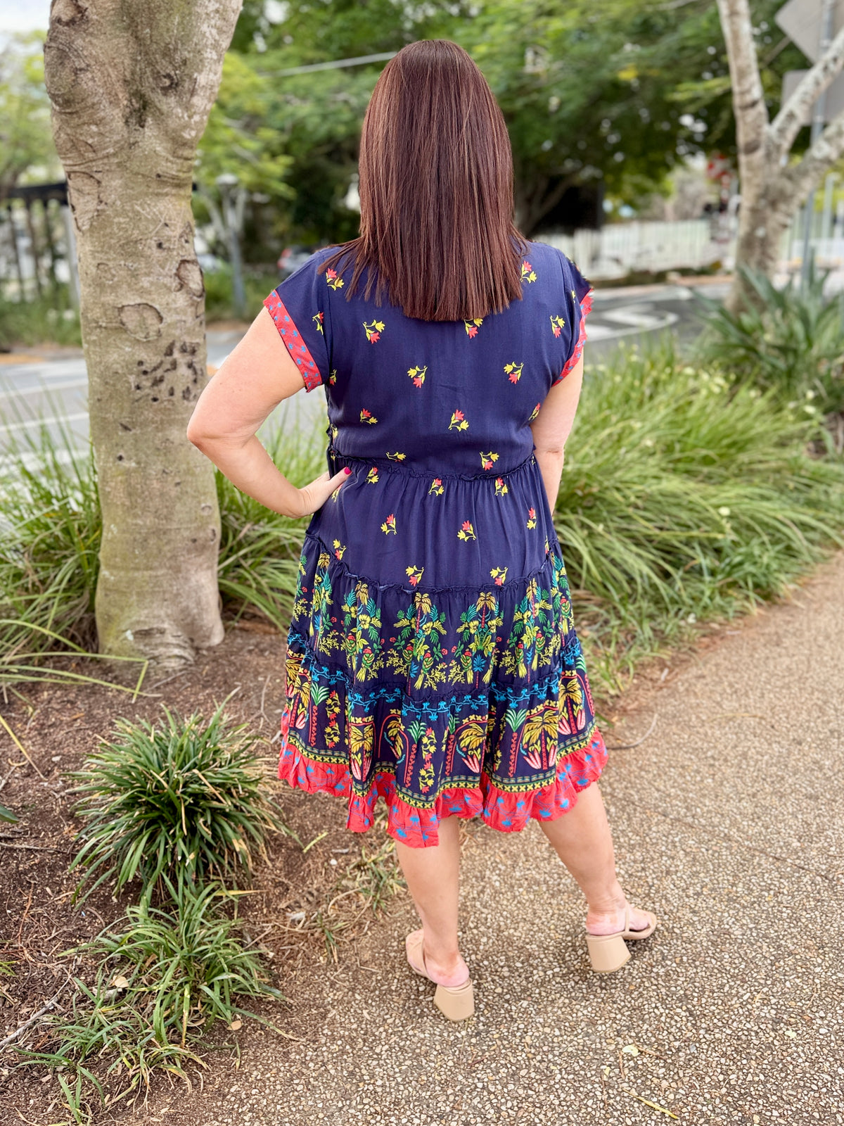 short-sleeve tiered dress with a navy blue base and coluorful bohemian-style floral and geometric patterns in red, green, yellow, and orange. The dress features a red and yellow patterned V-neckline and hem.