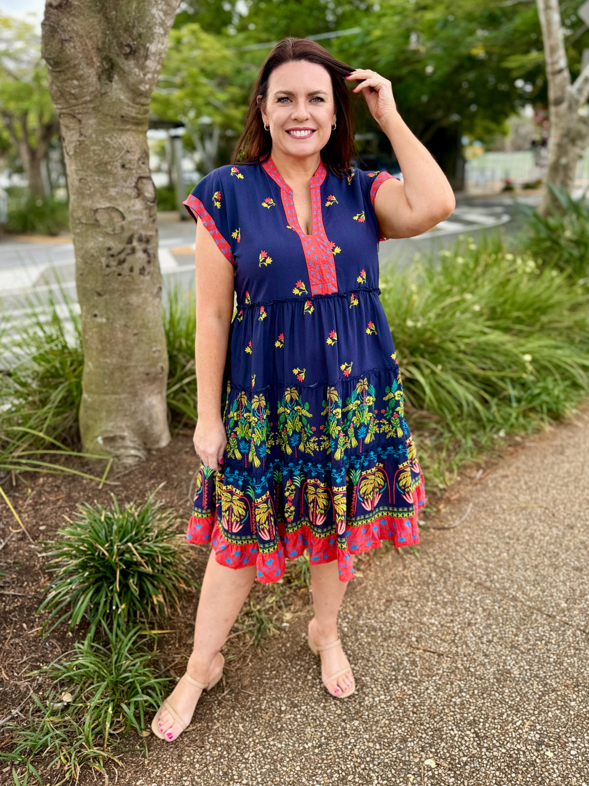short-sleeve tiered dress with a navy blue base and coluorful bohemian-style floral and geometric patterns in red, green, yellow, and orange. The dress features a red and yellow patterned V-neckline and hem.
