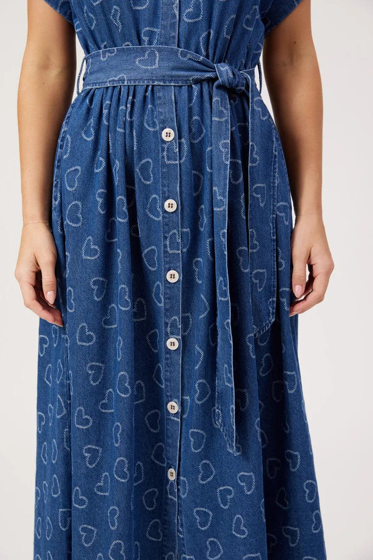 A close-up of a person wearing a blue denim-like dress with an allover white heart outline pattern, a matching waist tie, and a front button placket.