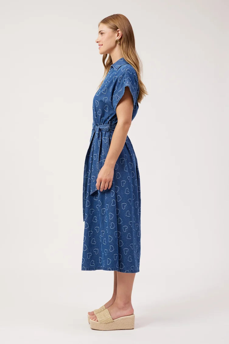 A woman stands in profile wearing a blue midi dress with a white heart pattern 