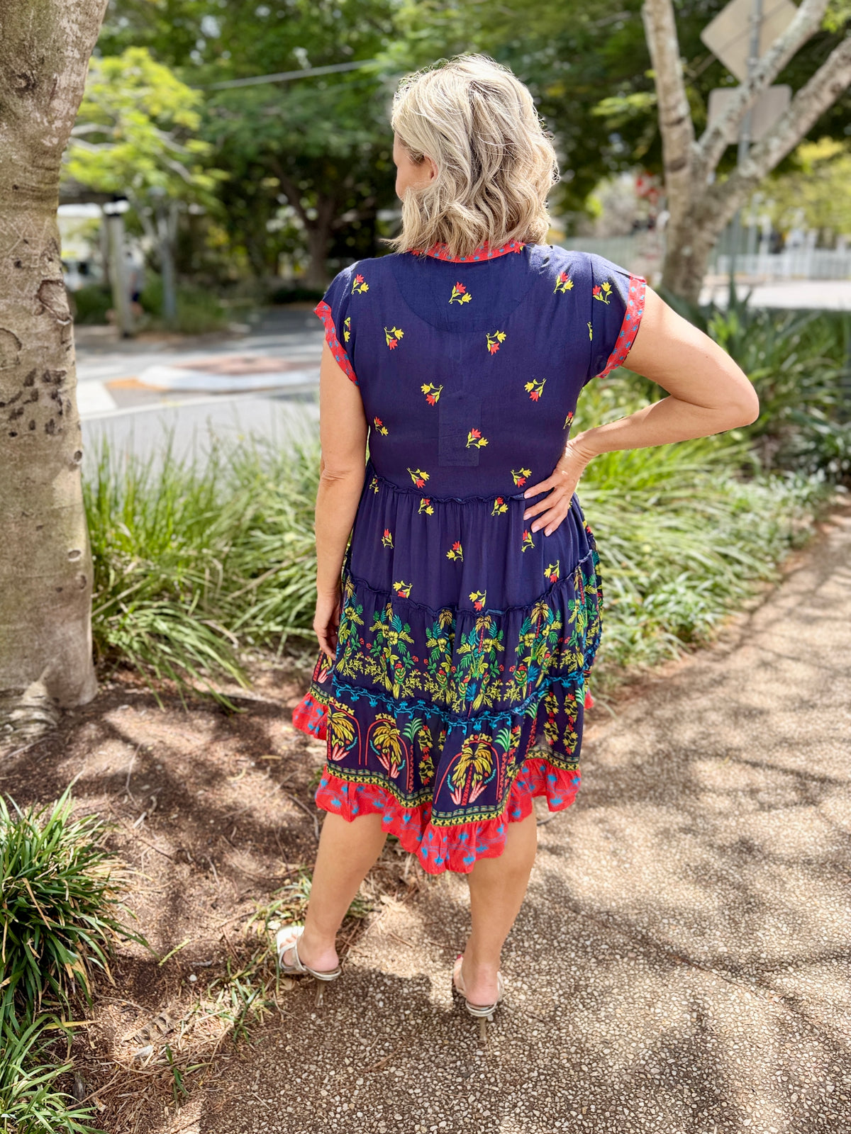 short-sleeve tiered dress with a navy blue base and coluorful bohemian-style floral and geometric patterns in red, green, yellow, and orange. The dress features a red and yellow patterned V-neckline and hem.