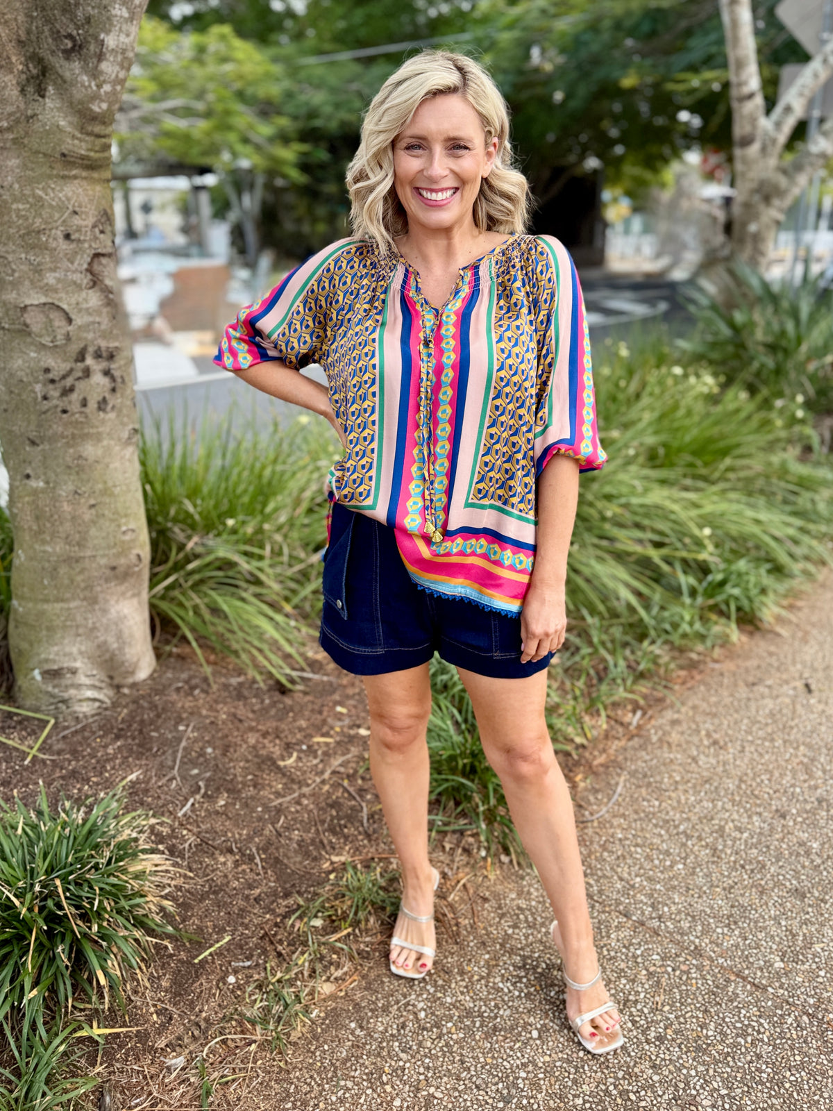 colorful patterned short-sleeve blouse with vertical stripes and dark navy shorts.