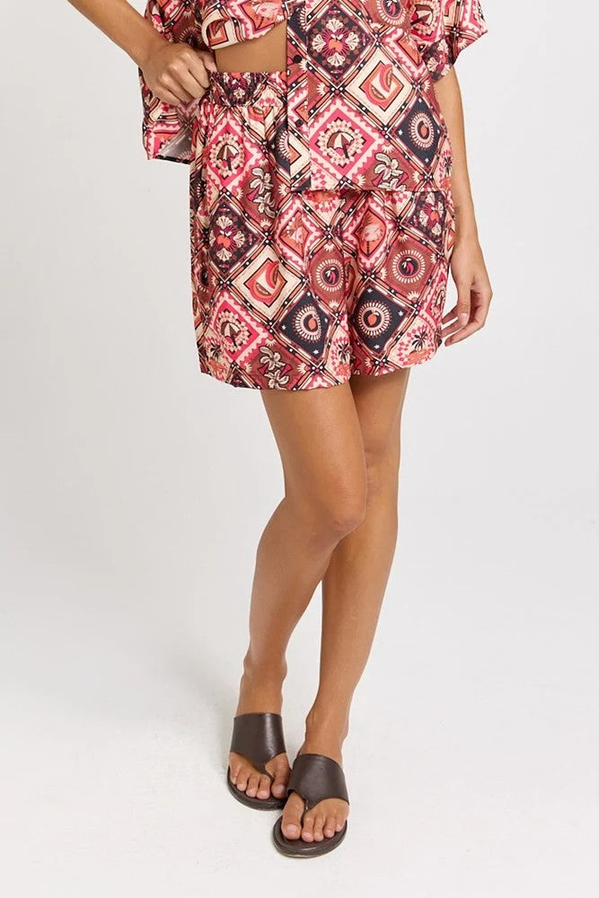 Matching set with short-sleeve collared shirt and  short with a colourful geometric and medallion pattern in red, pink, black, and white, 