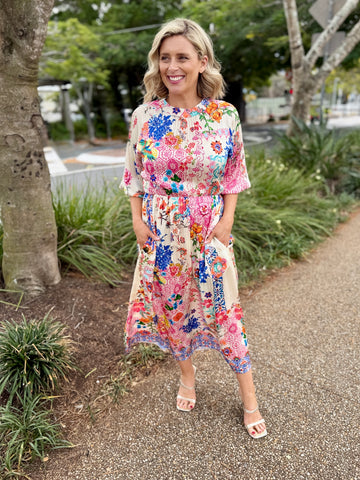A woman wearing a colorful floral midi dress with short sleeves and side pockets, 