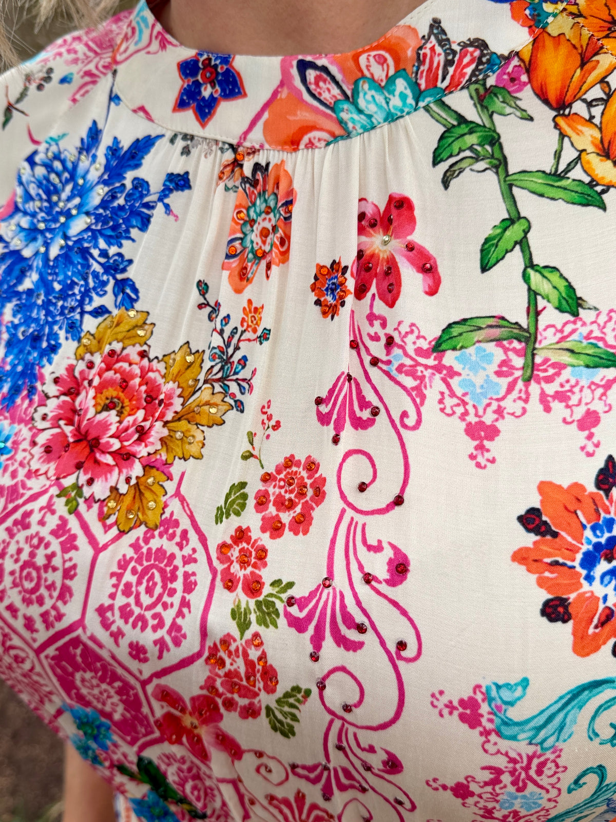 Close-up of a cream-colored blouse with a vibrant, multicolored floral and paisley print, featuring a gathered neckline.