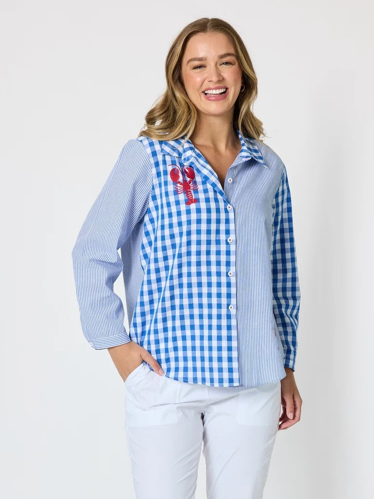 Women’s blue and white mixed‑pattern shirt featuring vertical stripes and gingham checks with red embroidered lobsters, styled with white pants — coastal casual outfit.