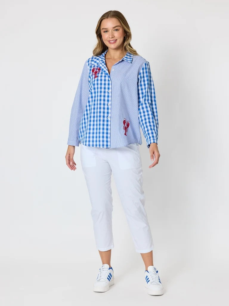 Women’s blue and white mixed‑pattern shirt featuring vertical stripes and gingham checks with red embroidered lobsters, styled with white pants — coastal casual outfit.