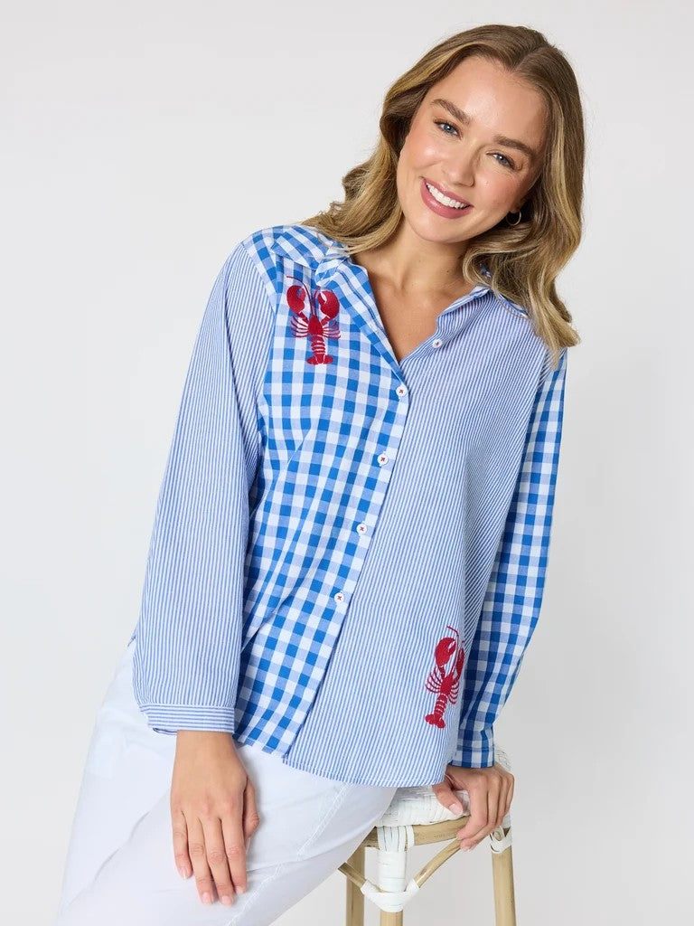 Women’s blue and white mixed‑pattern shirt featuring vertical stripes and gingham checks with red embroidered lobsters, styled with white pants — coastal casual outfit.