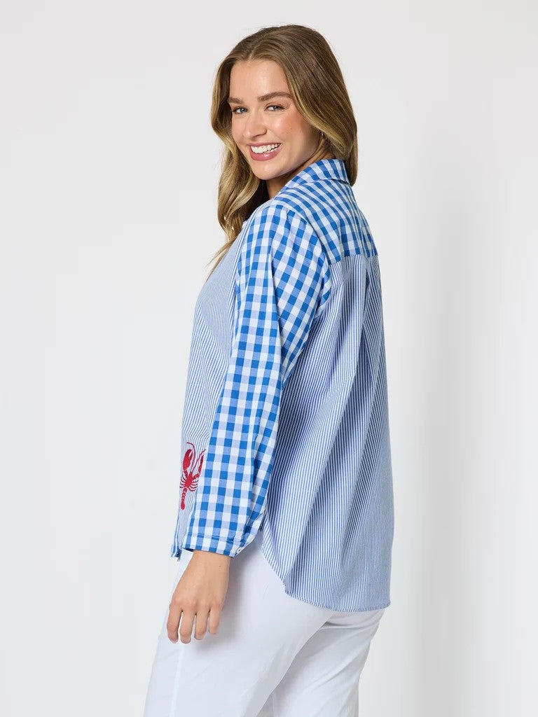 Women’s blue and white mixed‑pattern shirt featuring vertical stripes and gingham checks with red embroidered lobsters, styled with white pants — coastal casual outfit.