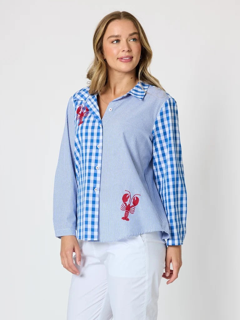 Women’s blue and white mixed‑pattern shirt featuring vertical stripes and gingham checks with red embroidered lobsters, styled with white pants — coastal casual outfit.
