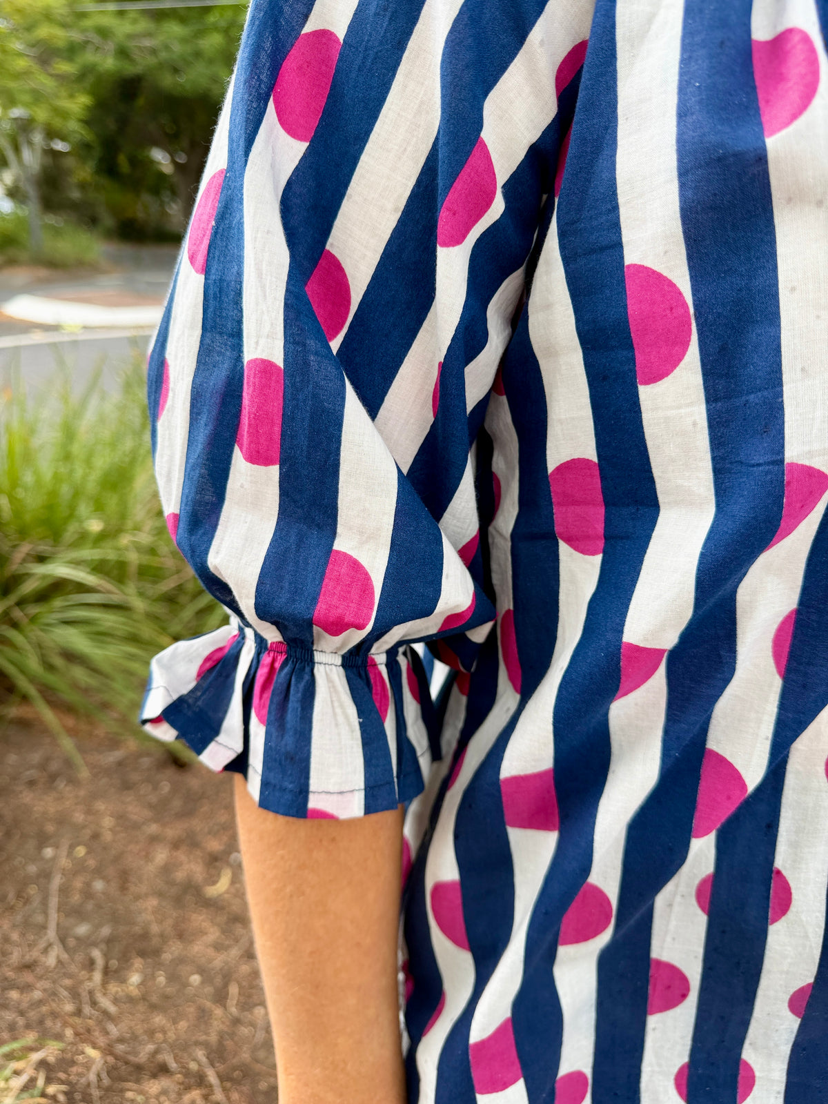  loose white shirt with navy blue vertical stripes and bright pink polka dots, with a ruffled elbow-length puff sleeve. 