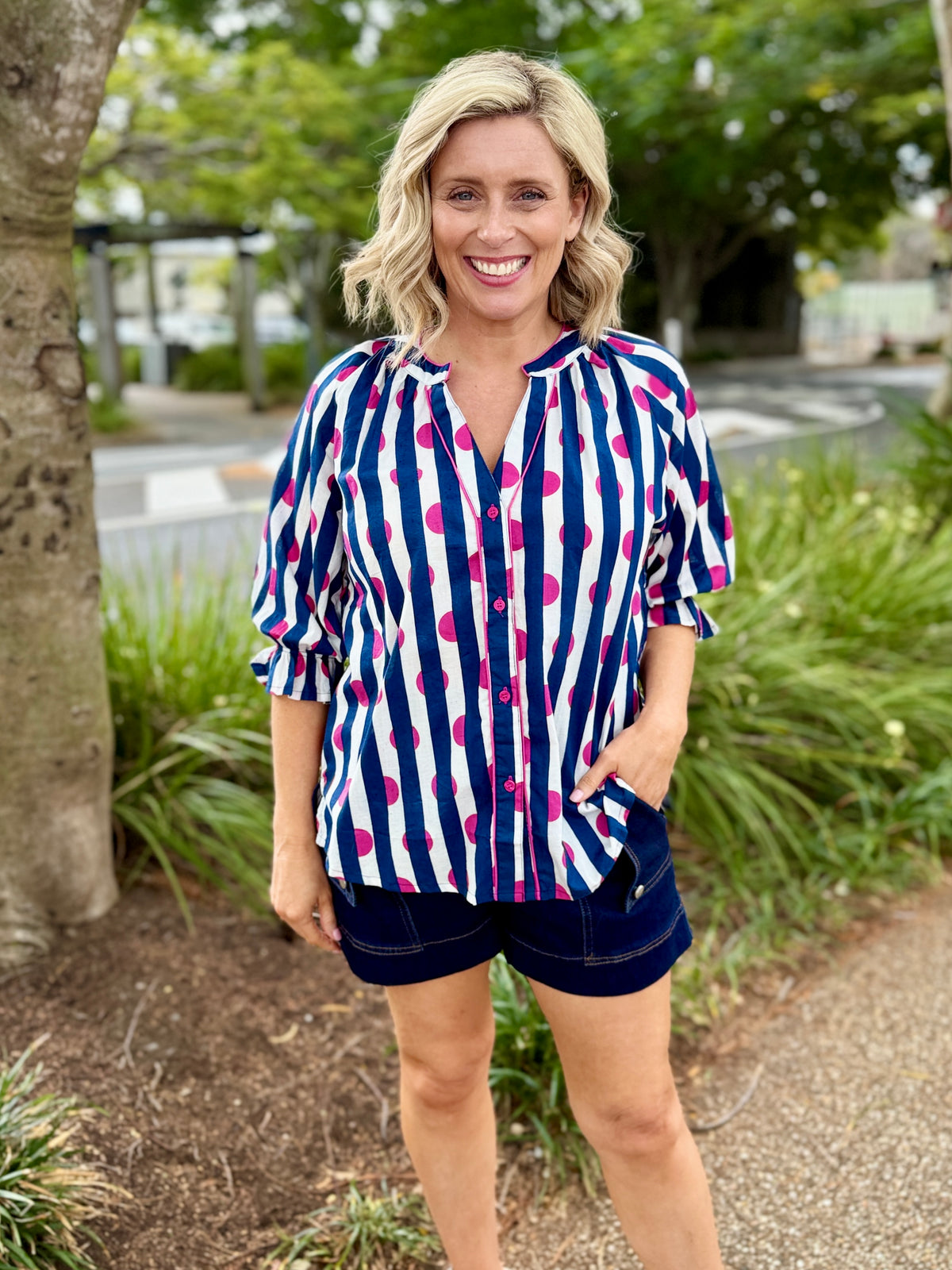 navy, white, and bright pink vertically striped button-up shirt with dark navy shorts.