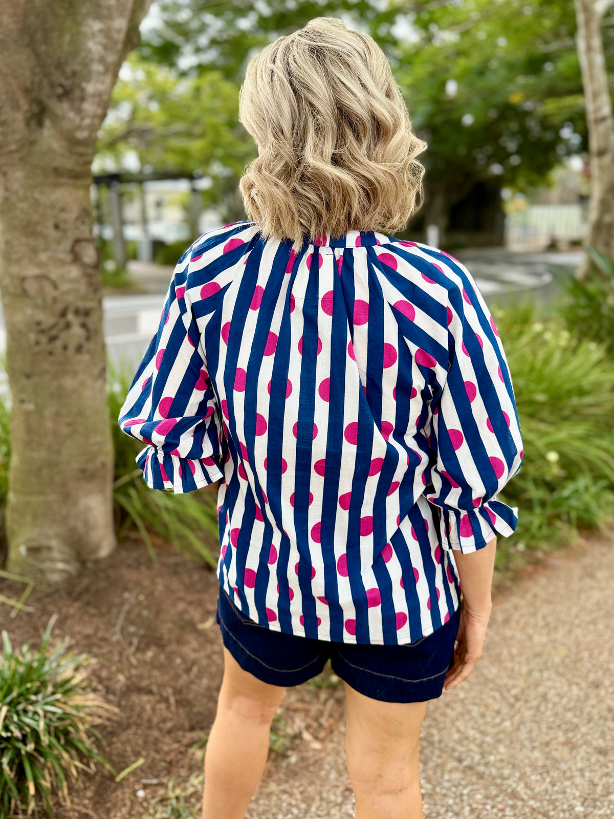 navy blue and white vertically striped blouse with bright pink polka dots, paired with dark navy shorts, 