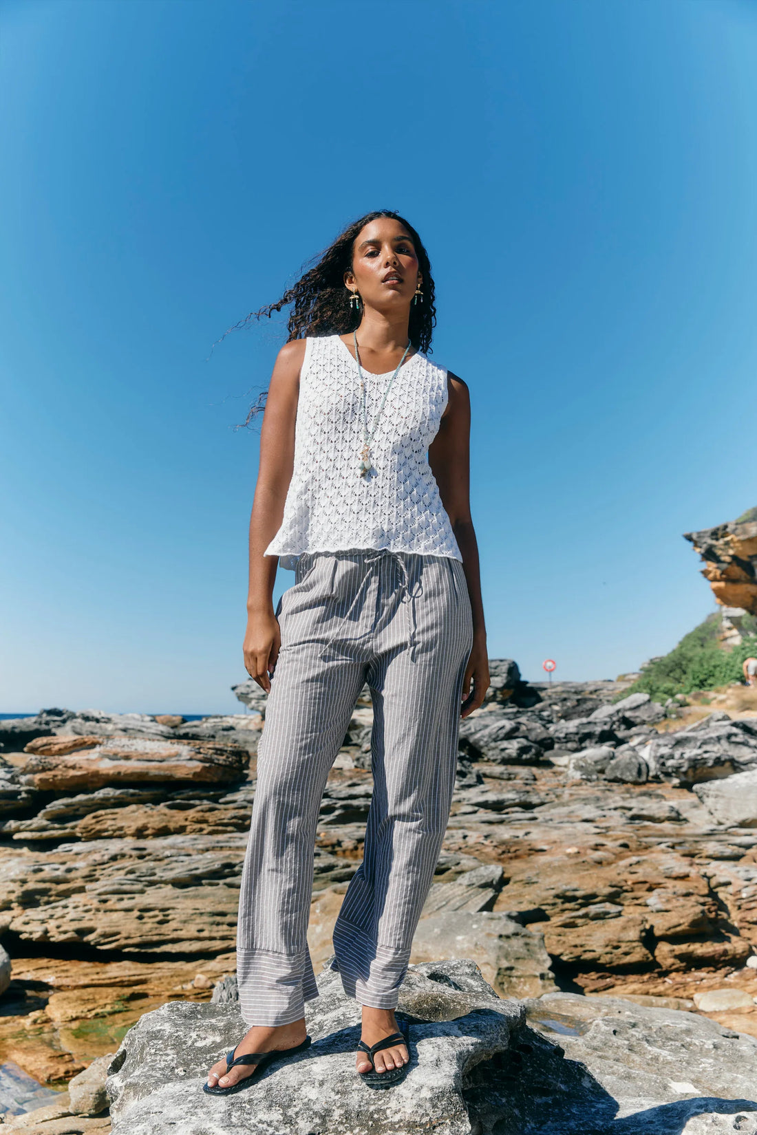 wearing a sleeveless white textured top and light grey pinstriped pants.