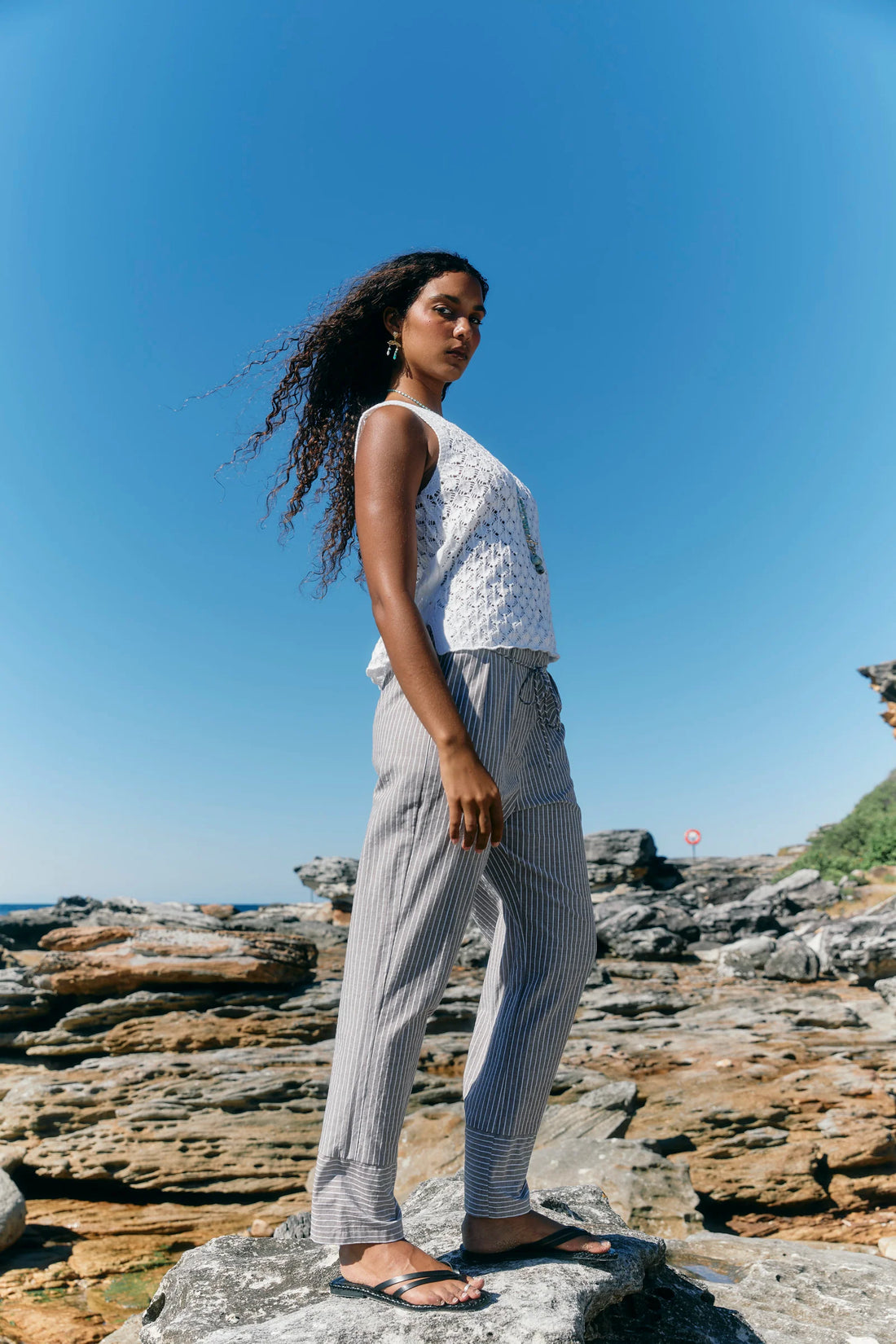 wearing a sleeveless white textured top and light grey pinstriped pants.