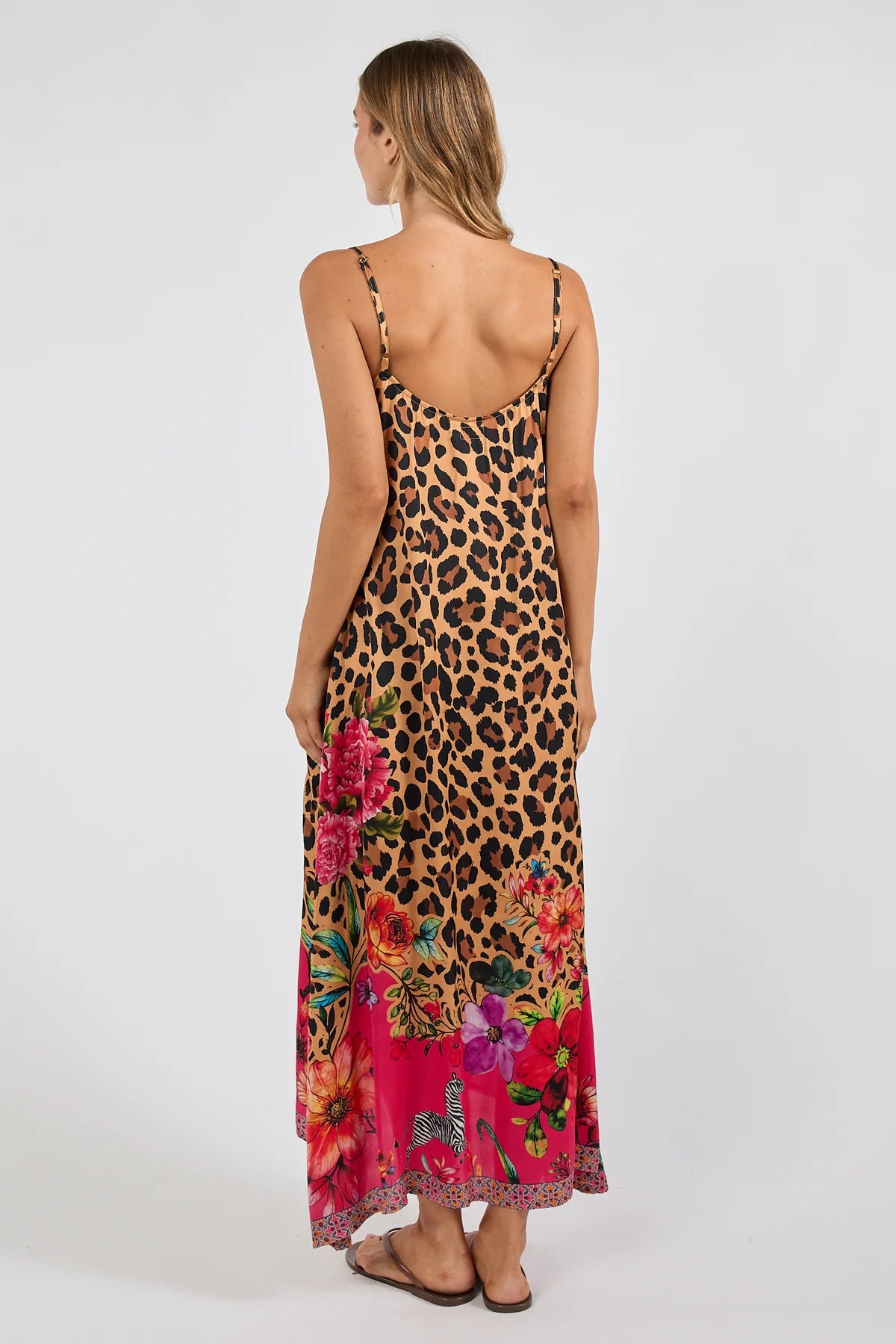 a sleeveless maxi dress with a leopard print base and a vibrant pink floral print along the hem and bodice. The dress features thin straps, a V-neckline with a multicolor embroidered pattern, and side pockets