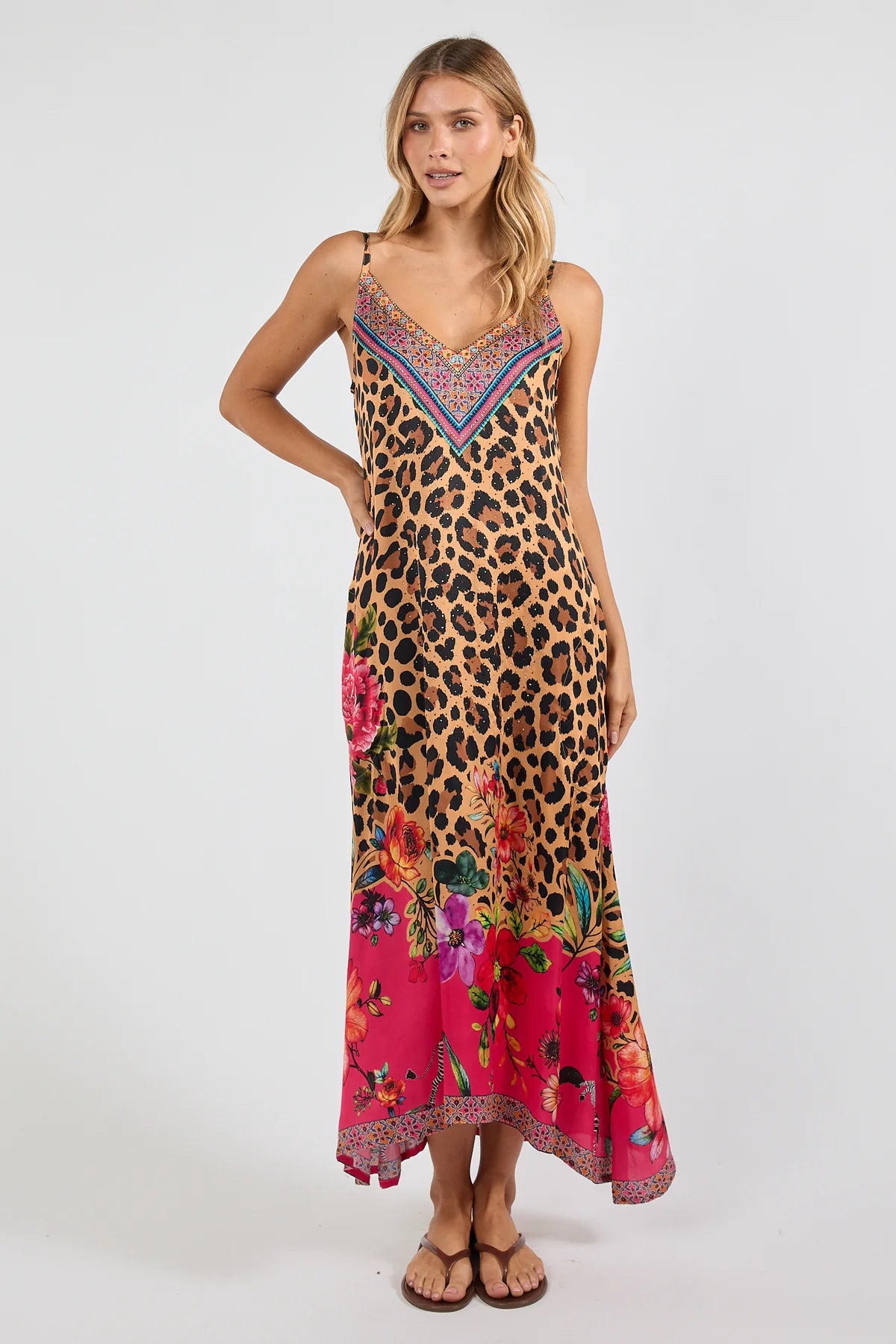 a sleeveless maxi dress with a leopard print base and a vibrant pink floral print along the hem and bodice. The dress features thin straps, a V-neckline with a multicolor embroidered pattern, and side pockets
